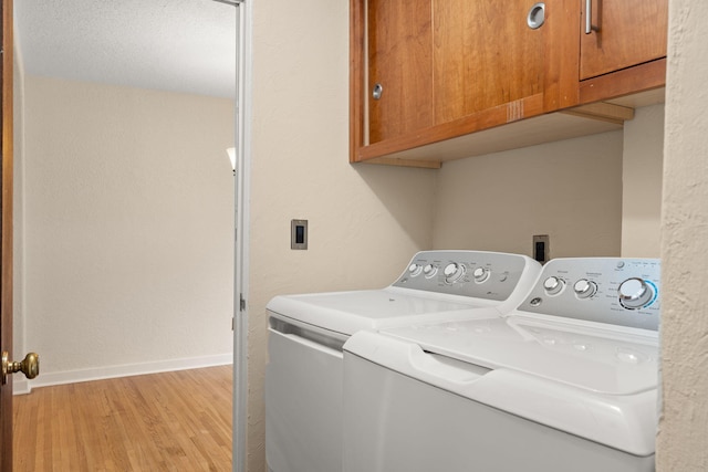 washroom featuring separate washer and dryer, cabinet space, a textured wall, light wood finished floors, and baseboards