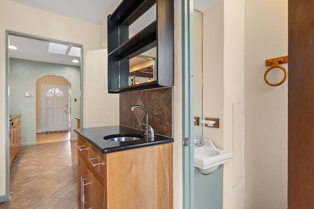 kitchen with open shelves, a sink, brown cabinets, arched walkways, and backsplash