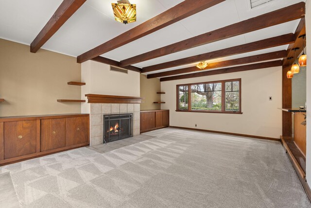 unfurnished living room with beamed ceiling, a tiled fireplace, visible vents, and carpet floors