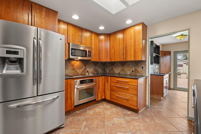 kitchen featuring brown cabinetry, dark countertops, backsplash, and appliances with stainless steel finishes