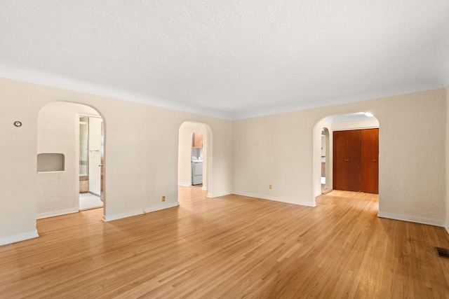 unfurnished living room featuring baseboards, arched walkways, washer / dryer, and light wood-type flooring