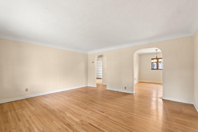 spare room featuring a textured ceiling, arched walkways, baseboards, light wood-style floors, and a notable chandelier