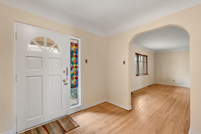 foyer with light wood-style flooring, baseboards, and arched walkways