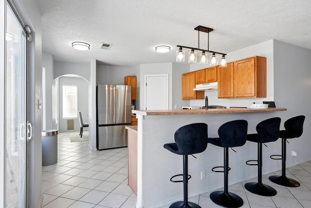 5909 Night Shadow Ave NW, Albuquerque, NM 87114 - kitchen featuring freestanding refrigerator, under cabinet range hood, arched walkways, a breakfast bar, and a peninsula