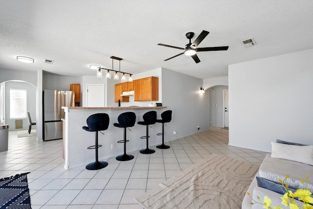 5909 Night Shadow Ave NW, Albuquerque, NM 87114 - kitchen with arched walkways, freestanding refrigerator, ceiling fan, a peninsula, and a breakfast bar area