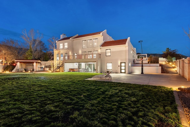 back of house at night featuring fence, stairs, a patio area, and stucco siding