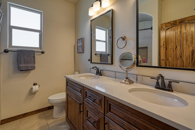 full bath featuring baseboards, a sink, double vanity, and toilet