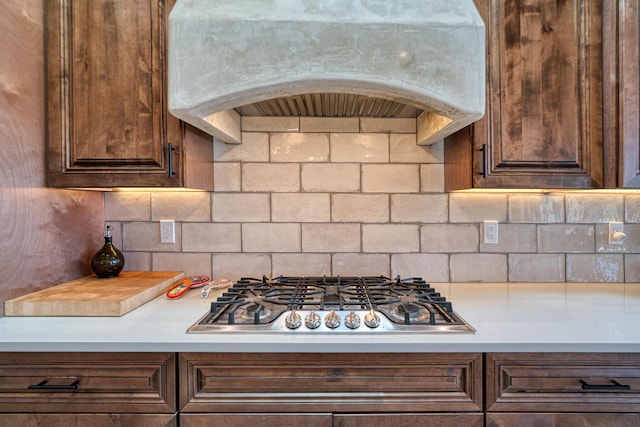 kitchen featuring dark brown cabinetry, stainless steel gas cooktop, light countertops, range hood, and tasteful backsplash