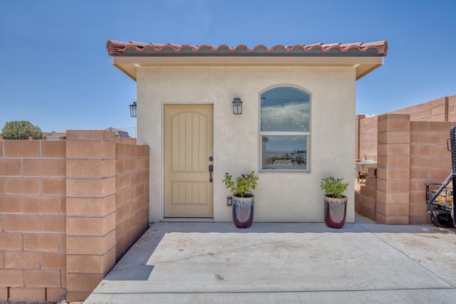 doorway to property featuring a tiled roof, fence, a patio area, and stucco siding