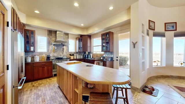 kitchen featuring recessed lighting, premium appliances, a kitchen island, wall chimney exhaust hood, and decorative backsplash