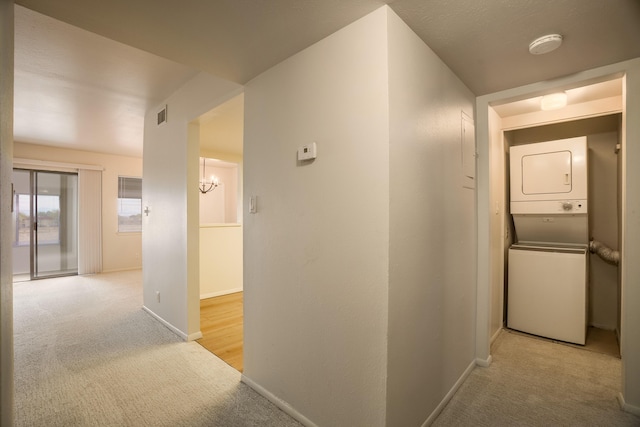 corridor featuring light colored carpet, baseboards, stacked washer / dryer, and visible vents