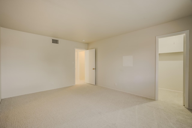 unfurnished bedroom featuring a spacious closet, light carpet, visible vents, and a closet