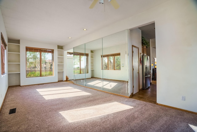 empty room with ceiling fan, carpet floors, visible vents, and baseboards
