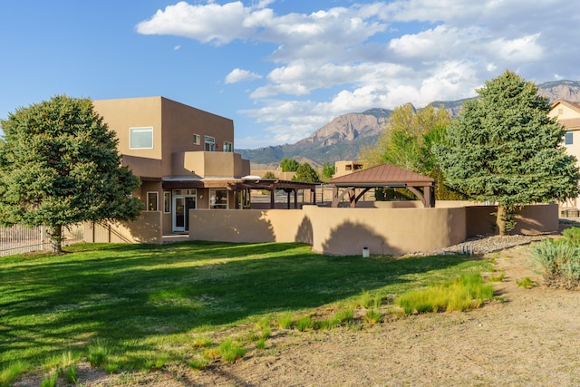 back of property with fence, stucco siding, a lawn, a gazebo, and a mountain view
