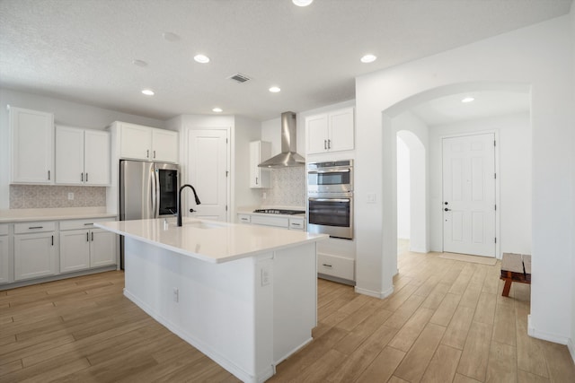 3003 Turquesa SE, Rio Rancho, NM 87124 - kitchen featuring a sink, wall chimney exhaust hood, appliances with stainless steel finishes, arched walkways, and light wood-type flooring