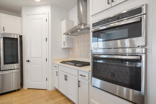 3003 Turquesa SE, Rio Rancho, NM 87124 - kitchen featuring wall chimney exhaust hood, appliances with stainless steel finishes, light wood-type flooring, decorative backsplash, and white cabinets