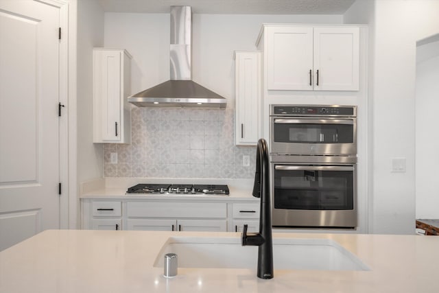 3003 Turquesa SE, Rio Rancho, NM 87124 - kitchen featuring wall chimney exhaust hood, stainless steel appliances, light countertops, decorative backsplash, and white cabinetry
