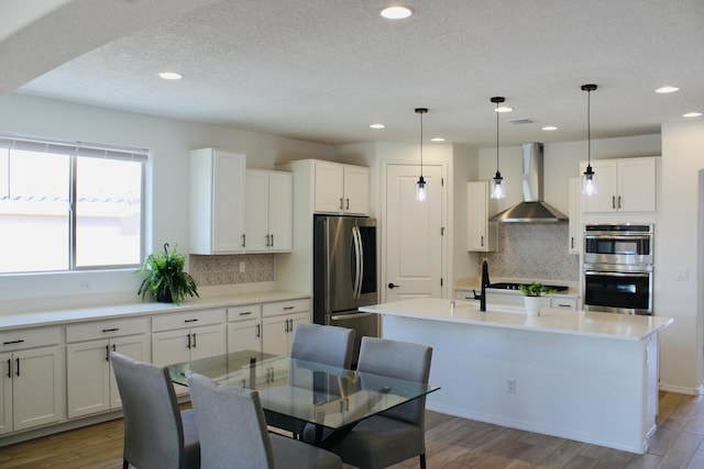 3003 Turquesa SE, Rio Rancho, NM 87124 - kitchen with wall chimney exhaust hood, appliances with stainless steel finishes, a kitchen island with sink, backsplash, and a textured ceiling