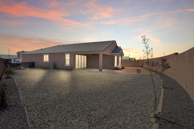 3003 Turquesa SE, Rio Rancho, NM 87124 - back of house at dusk featuring central AC, a patio area, a fenced backyard, a tiled roof, and stucco siding