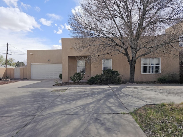 pueblo-style house featuring stucco siding, an attached garage, fence, and concrete driveway