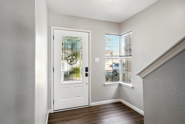 foyer entrance featuring dark wood finished floors, a textured wall, and baseboards