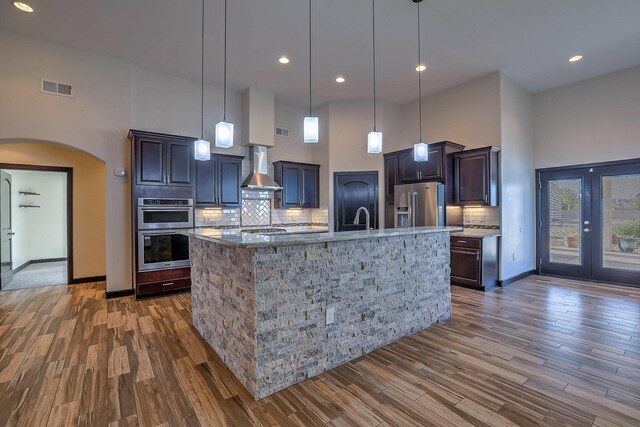 1797 Vargas Rd SE, Rio Rancho, NM 87124 - kitchen featuring a high ceiling, arched walkways, stainless steel appliances, dark wood-style flooring, and wall chimney range hood