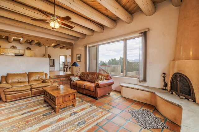 living area featuring a ceiling fan, light tile patterned floors, a large fireplace, beamed ceiling, and wooden ceiling