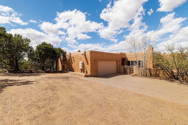 pueblo-style home featuring an attached garage, decorative driveway, and fence private yard
