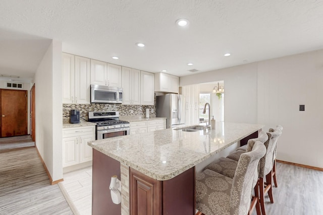 kitchen with a kitchen breakfast bar, a sink, decorative backsplash, a kitchen island with sink, and stainless steel appliances