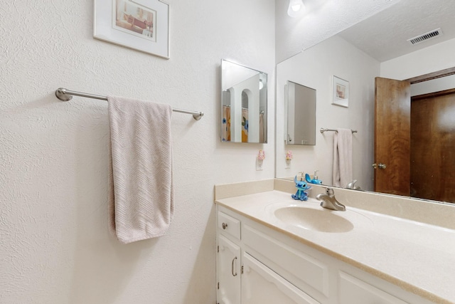 bathroom featuring a textured wall, visible vents, and vanity