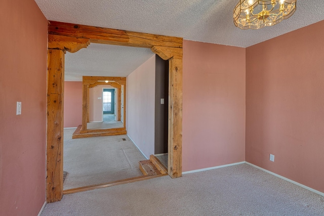 carpeted spare room featuring a textured ceiling, a chandelier, and baseboards