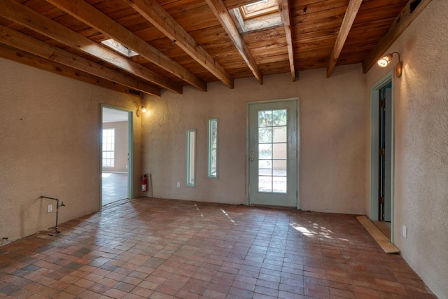 empty room featuring wooden ceiling, beam ceiling, brick flooring, a textured wall, and a skylight