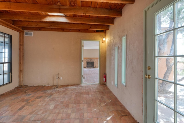 unfurnished room featuring wood ceiling, beam ceiling, and brick patterned flooring