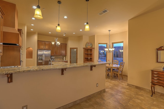 255 Diamond Tail Rd, Placitas, NM 87043 - kitchen with a chandelier, stainless steel refrigerator with ice dispenser, a kitchen bar, light stone counters, and brown cabinetry