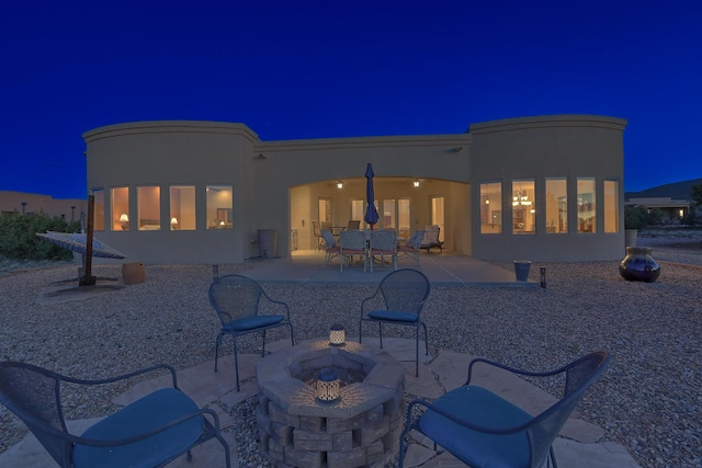 back of house at twilight with stucco siding, a fire pit, and a patio area