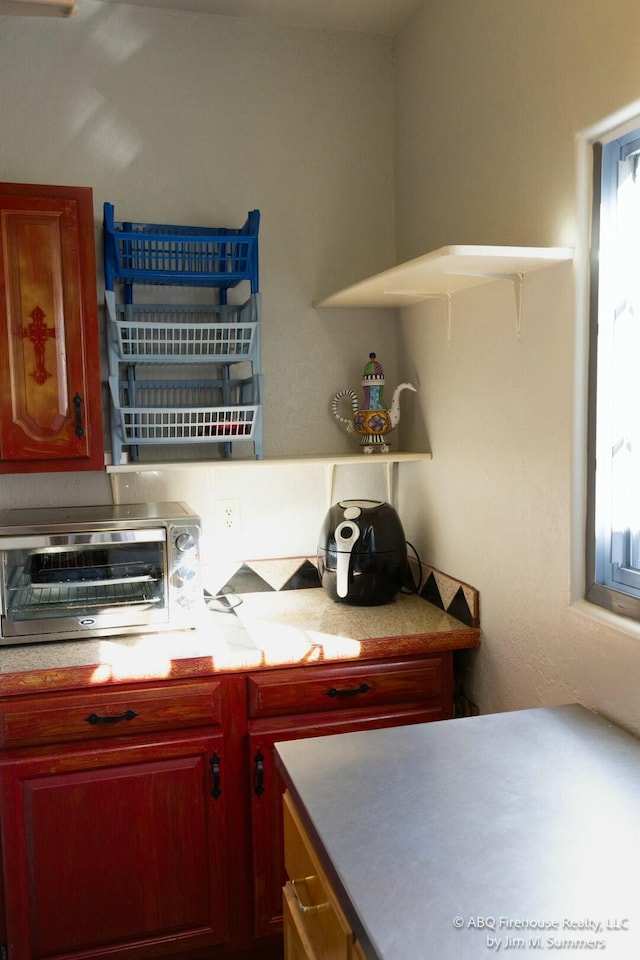 kitchen featuring a toaster, reddish brown cabinets, and light countertops