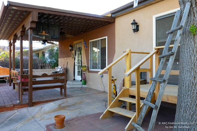 doorway to property featuring fence, ceiling fan, stucco siding, and a patio area