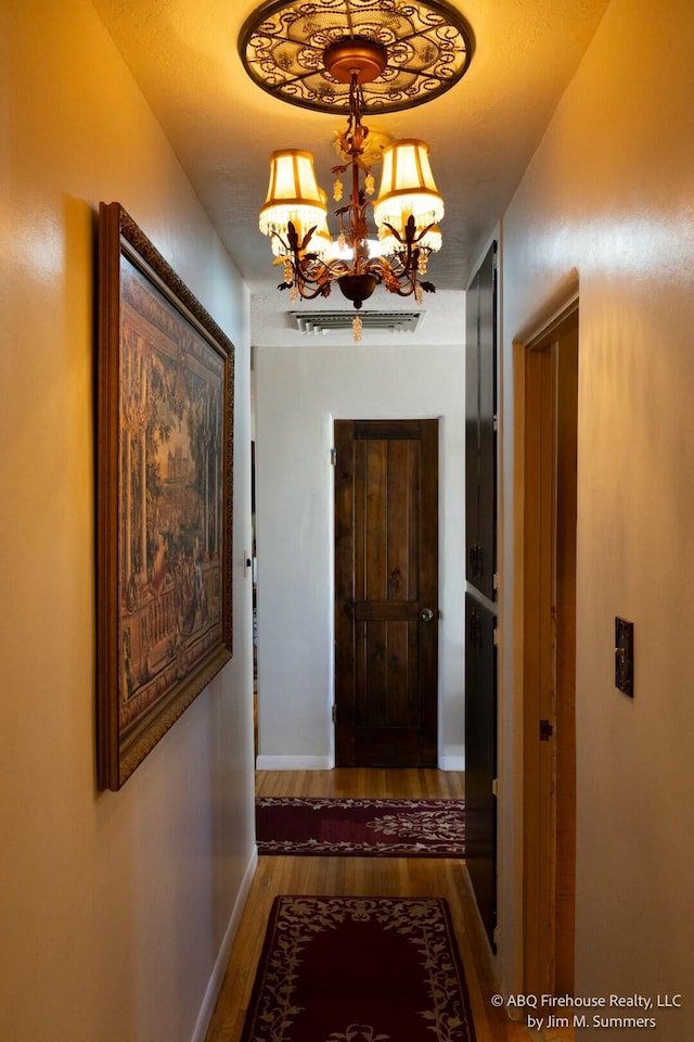 hallway featuring baseboards, wood finished floors, and an inviting chandelier
