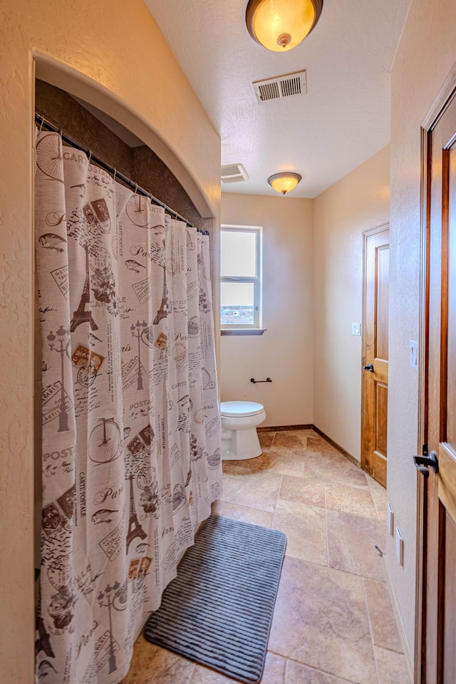 5016 Frontier Rd NE, Rio Rancho, NM 87144 - bathroom featuring stone tile flooring, toilet, baseboards, visible vents, and curtained shower