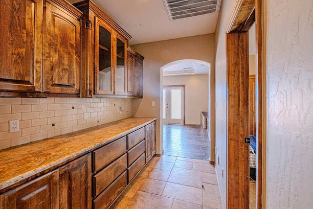5016 Frontier Rd NE, Rio Rancho, NM 87144 - kitchen with light stone counters, visible vents, arched walkways, decorative backsplash, and glass insert cabinets