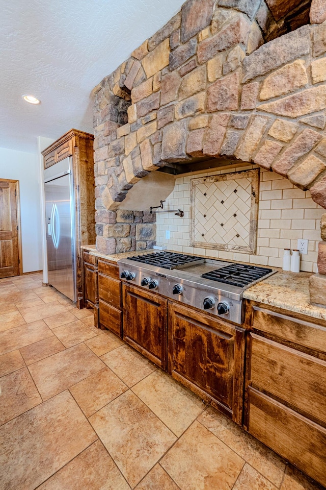 5016 Frontier Rd NE, Rio Rancho, NM 87144 - kitchen with a textured ceiling, brown cabinets, stainless steel appliances, backsplash, and light stone countertops