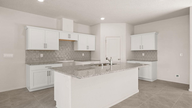 kitchen featuring a sink, decorative backsplash, an island with sink, and white cabinetry