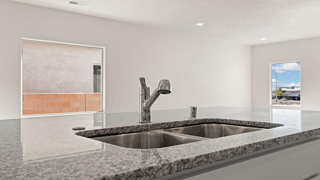 interior details with a textured ceiling, visible vents, a sink, stone counters, and recessed lighting