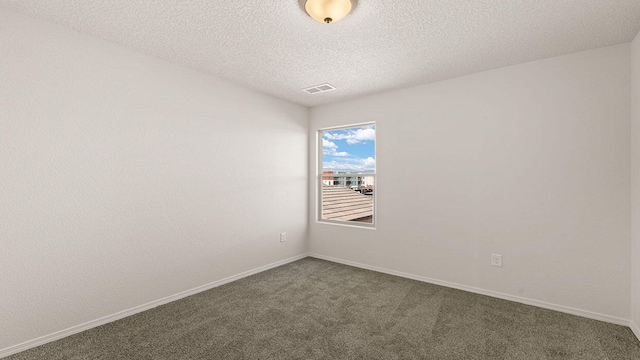 empty room with dark colored carpet, a textured ceiling, baseboards, and visible vents
