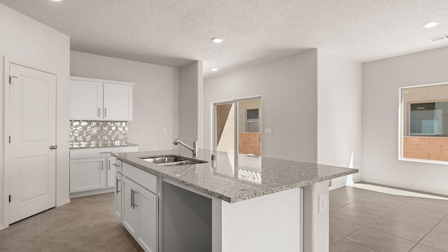 kitchen featuring light tile patterned floors, light stone countertops, white cabinetry, and a sink