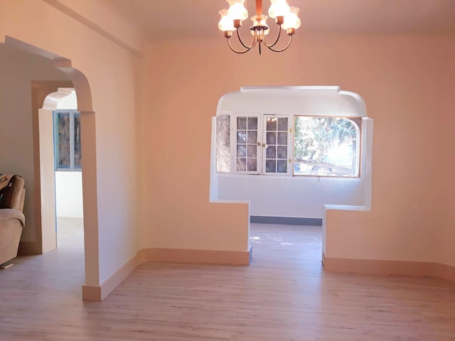 interior space featuring wood finished floors, baseboards, arched walkways, and a notable chandelier