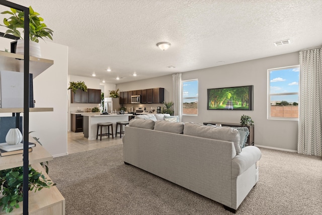 living area featuring recessed lighting, visible vents, baseboards, a textured ceiling, and light colored carpet