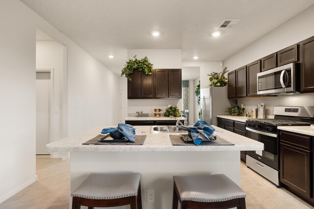 kitchen featuring a sink, dark brown cabinets, visible vents, a breakfast bar, and appliances with stainless steel finishes