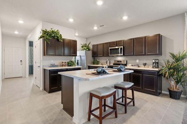 kitchen featuring a kitchen bar, dark brown cabinetry, stainless steel appliances, and light countertops