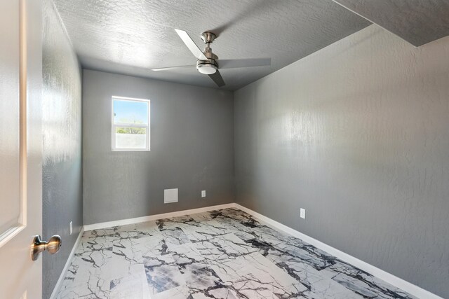empty room with marble finish floor, baseboards, a textured ceiling, and ceiling fan